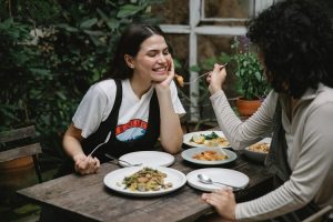 Two people enjoying a meal at an outdoor kitchen table, one feeding the other.