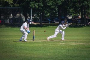 A cricketer swings his bat, focused and determined, in the heart of the game.