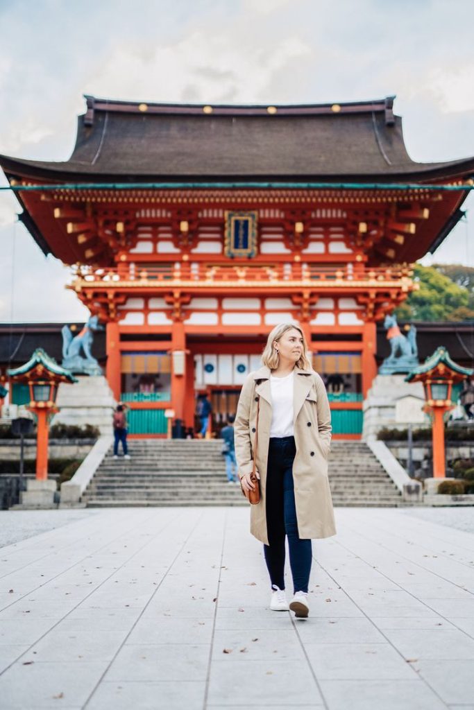 Traditional Japanese pagoda nestled among cherry blossoms, with a woman traveler capturing the beauty of Japanese culture.